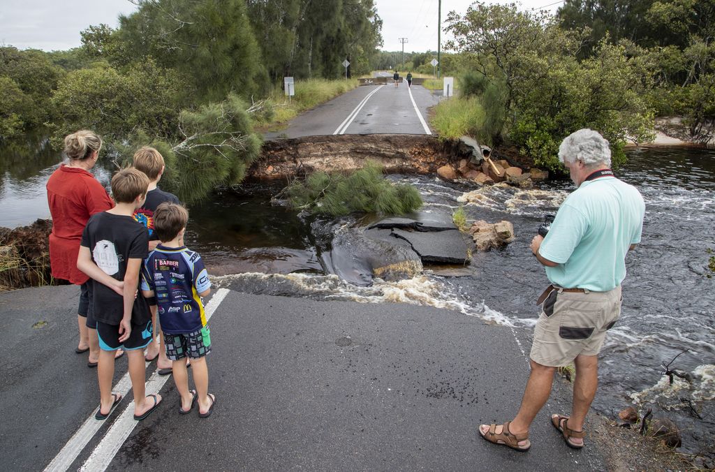 People stand at a washed out section of road at Port Stephens 200 kilometers (124 miles) north of Sydney, Australia, Saturday, March 20, 2021. People across New South Wales have been warned to expect intense rain and potentially life-threatening flooding, with Sydney predicted to be deluged with up to 200 millimeters of rain in one day. (AP Photo/Mark Baker)