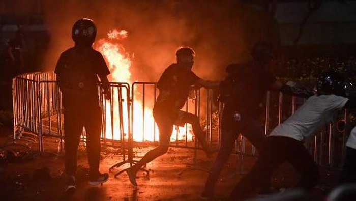 Pengunjuk rasa pro-demokrasi mencoba untuk menghapus pagar barikade di samping api dari bom molotov yang dilemparkan selama bentrokan dengan polisi anti huru hara pada demonstrasi anti-pemerintah di Bangkok pada 20 Maret 2021. (Lillian Suwan/AFP)