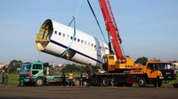 Bagian-bagian pesawat diangkat menggunakan alat berat.