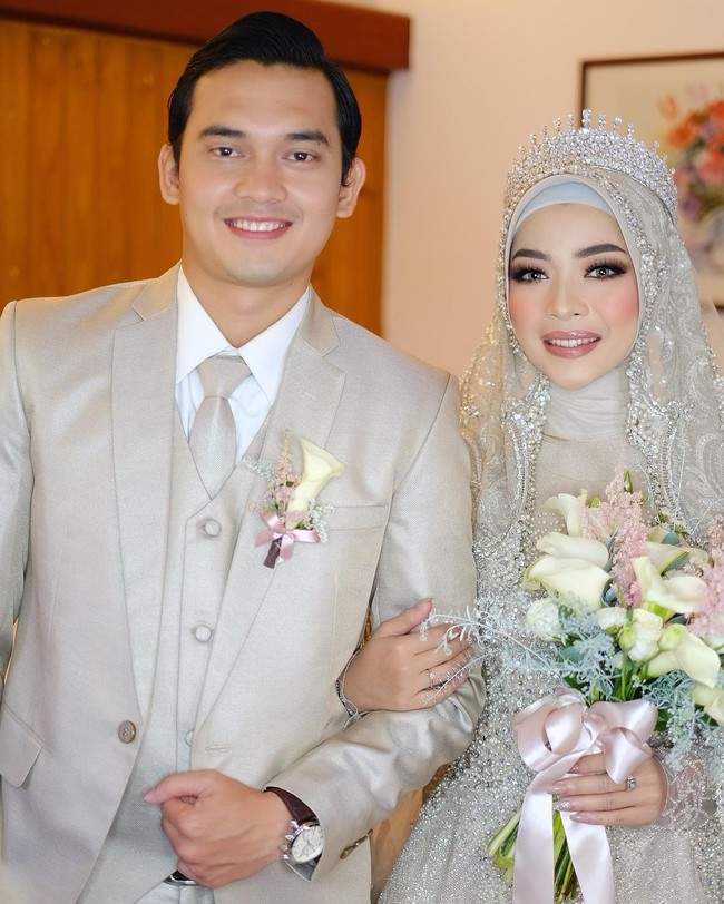 Saat resepsi pernikahan, Novia tampak memakai hijab chiffon babydoll yang dililit rapi ke belakang dan dilengkapi dengan inner hijab bahan kaus agar bagian rambut tidak terlihat. Gaya hijab ini akan mempercantik hiasan headpiece mahkota dan wedding veil.  Foto: Instagram: @luckyhakim9