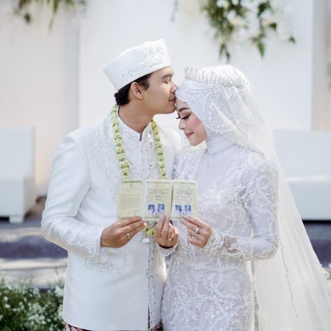 Pada saat acara akad nikah, Ikbal dan Novia memakai busana serba putih. Keduanya berpose memperlihatkan buku nikah, sementara Ikbal mencium kening Novia.  Foto: Dok. Instagram @ikbalicious_ofc.