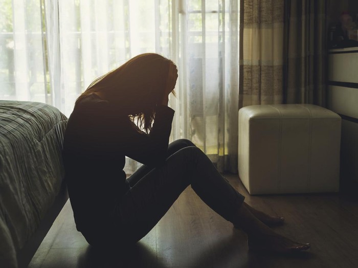 depressed woman sitting head in hands in the dark bedroom