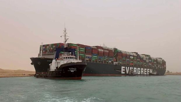 In this photo released by the Suez Canal Authority, a boat navigates in front of a massive cargo ship, named the Ever Green, rear, sits grounded Wednesday, March 24, 2021, after it turned sideways in Egypt’s Suez Canal, blocking traffic in a crucial East-West waterway for global shipping. An Egyptian official warned Wednesday it could take at least two days to clear the ship. (Suez Canal Authority via AP)