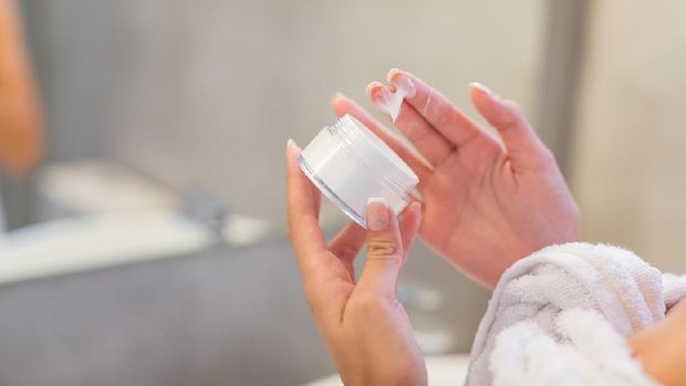 Hand holding a facial cream jar and taking cream out with fingers
