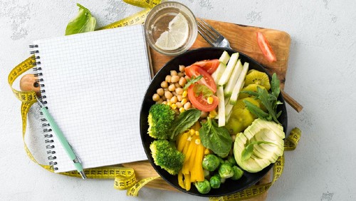 Vegan healthy balanced diet concept. Vegetarian buddha bowl with blank notebook and measuring tape. hickpeas, broccoli, pepper, tomato, spinach, arugula and avocado in plate on white background. Top view