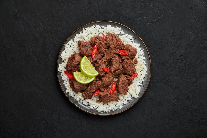 Beef Rendang on black plate at black slate table top. Indonesian padang cuisine meat dish. Asian food. Top view