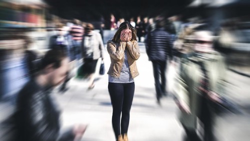 Panic attack in public place. Woman having panic disorder in city. Psychology, solitude, fear or mental health problems concept. Depressed sad person surrounded by people walking in busy street.