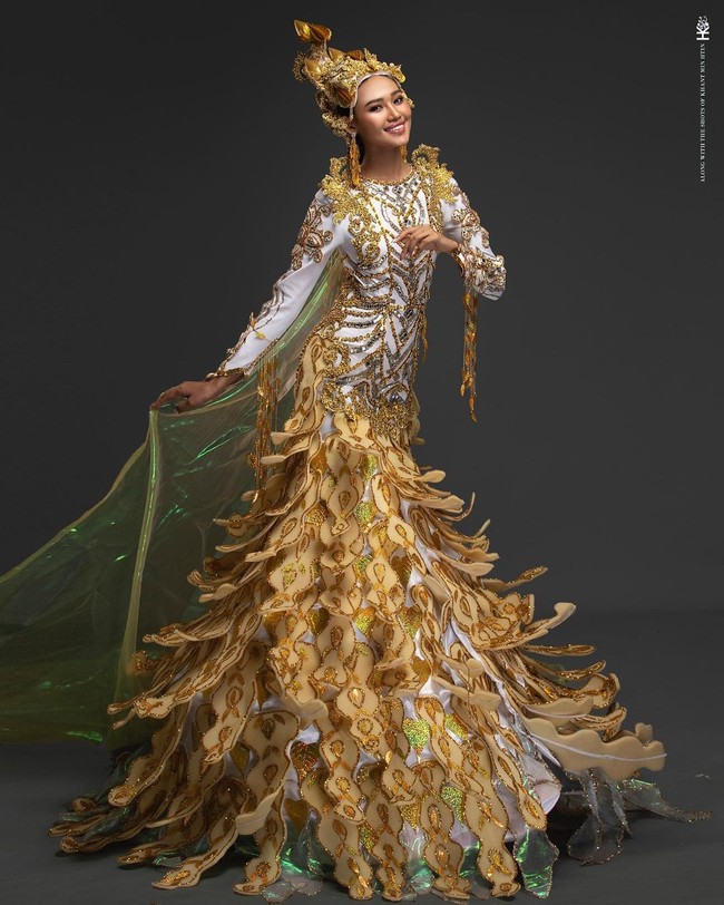 Kostum nasional yang dibawakan oleh Miss Grand Myanmar, Han Lay, bertajuk A Goddess of Peace. Kostum yang didominasi warna kuning keemasan dan putih itu melambangkan kedamaian yang dibutuhkan oleh dunia. Kostum itu dibuat dengan refleksi dari Dewi Perdamaian yang memercikkan air mata cinta dengan tangkai Aung Tha Pyae (Eugenia) dan melambangkan kemenangan perdamaian dengan ornamen Myanmar. Foto: Instagram/@hann_may