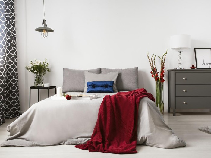 Real photo of a romantic bedroom interior with a big bed, red blanket, rose and commode