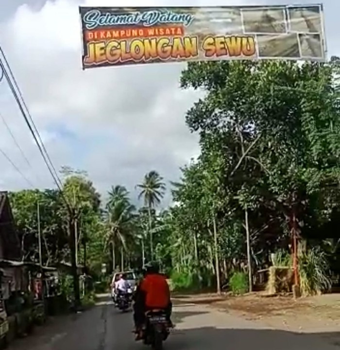 Sebuah spanduk bertuliskan Selamat Datang ke Kampung Wisata Jeglongan Sewu terpasang di jalan. Spanduk itu bentuk kegeraman warga karena laporan mereka soal kerusakan jalan tak mendapat tanggapan dari pemerintah.