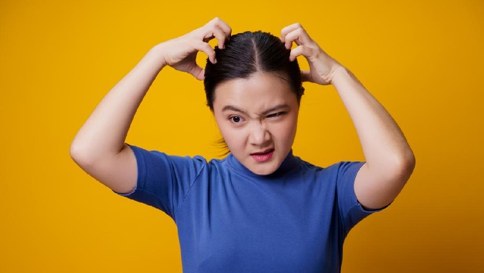 Asian woman bored and annoyed, scratching her head, isolated on yellow background.