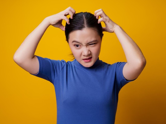Asian woman bored and annoyed, scratching her head, isolated on yellow background.