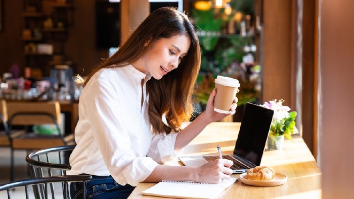 Quarantine Young asian woman wearing smart casual clothes work at home in living room using laptop and drinking hot coffee and croissant while city  lockdown for covid-19 corona virus pandemic.