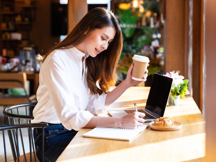 Ilustrasi Wanita Karier Quarantine Young asian woman wearing smart casual clothes work at home in living room using laptop and drinking hot coffee and croissant while city lockdown for covid-19 corona virus pandemic.