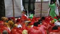 Para peserta aksi mengenakan jas hujan dari plastik yang difungsikan sebagai alat pelindung diri (APD) dengan warna merah, hijau, dan biru.  
