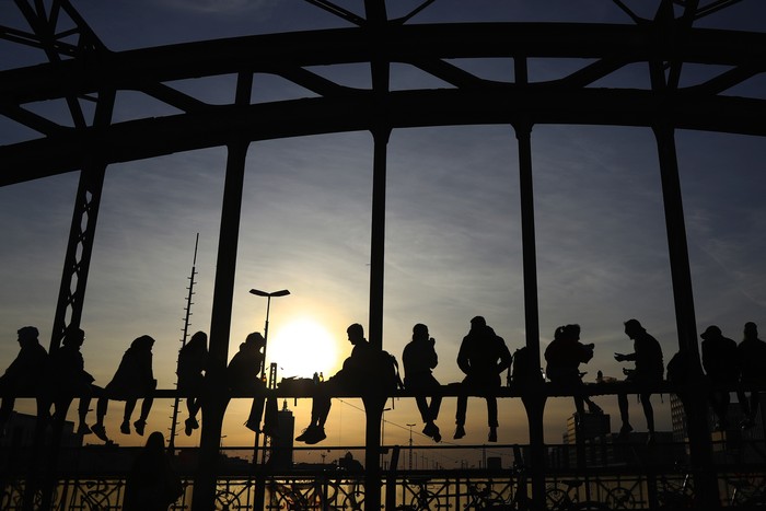 Young people enjoy the sunset at the bridge 'Hackerbruecke' in Munich, Germany, Sunday, March 28, 2021. (AP Photo/Matthias Schrader)