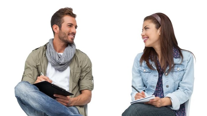 Full length of a cool young couple writing in notepads over white background