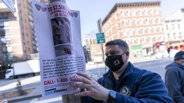 A police officer hangs a sign offering a reward for information on the person who attacked an Asian American woman near the crime scene, Tuesday, March 30, 2021, in New York. The New York City Police Department says an Asian American woman was attacked by a man Monday afternoon who repeatedly kicked her in front of witnesses who seemingly stood by. (AP Photo/Mary Altaffer)