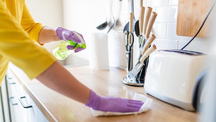 Hands in gloves disinfecting kitchen counter and wiping with paper towel against viruses