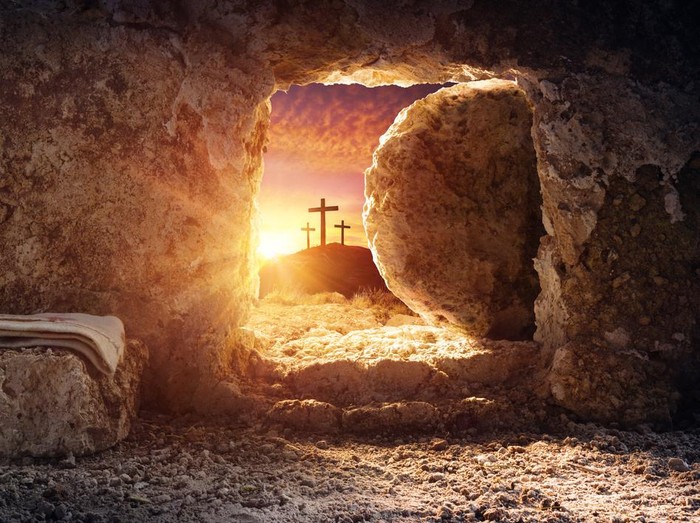 Empty tomb of Jesus at sunrise with crosses in background