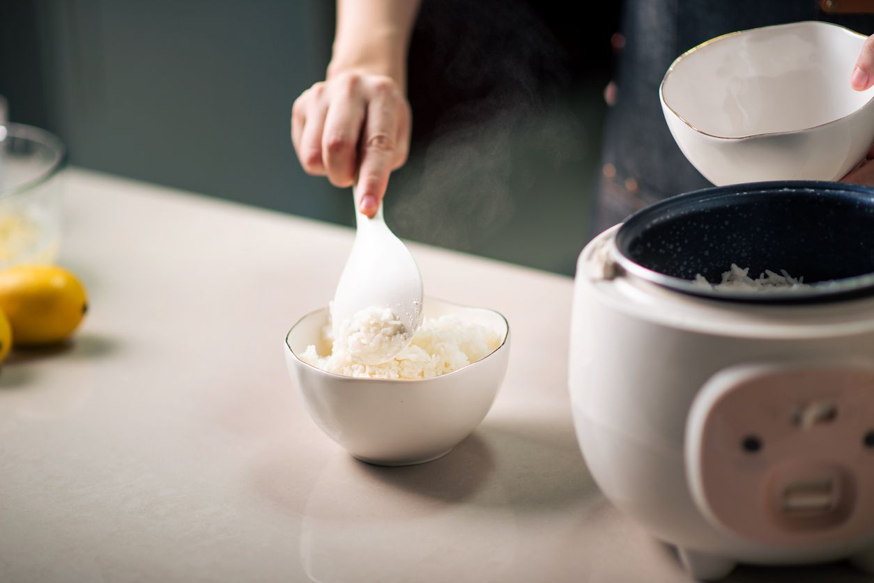 Woman taking out and serving fresh boiled fragrant jasmine rice from the rice cooker in the kitchen at home