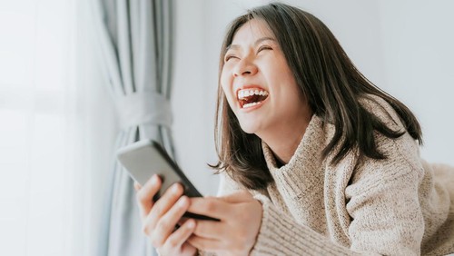 Ilustrasi seseorang yang sedang tertawa saat membaca pesan singkat.