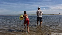 Seorang anak bermain di pantai bersama orang tuanya.