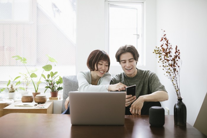 Ilustrasi menggunakan ponsel Couple sitting behind a coffee table, installing virtual assistant.