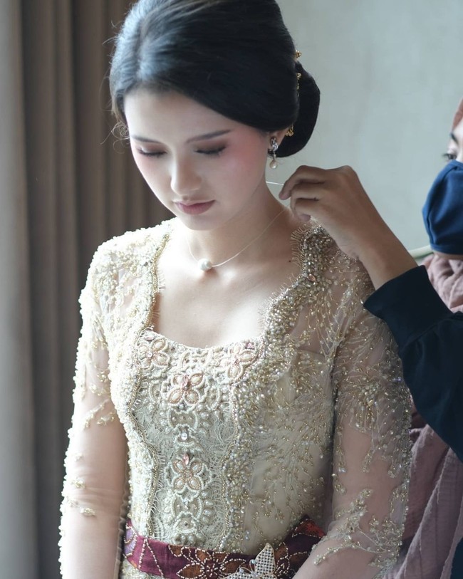 Anak dari pemilik resort di Bali ini mengenakan kebaya modern dari Windy Savosa Couture. Kebaya bernuansa champagne dipercantik dengan ikat pinggang dari tenun ikat yang dihias bros kupu-kupu. Foto: Instagram/@ssarah_menzel, @estherkwanmua