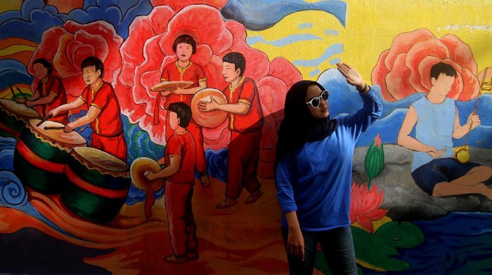Seorang warga berpose di depan lukisan mural di dinding rumah toko di Gajahmada 9, Pontianak, Kalimantan Barat, Selasa (6/4/2021). Mural yang menggambarkan kesenian Tionghoa dan diinisiasi oleh pegiat seni Hervin Yulianto tersebut menjadi salah satu destinasi wisata baru di Kota Pontianak. ANTARA FOTO/Jessica Helena Wuysang/wsj.