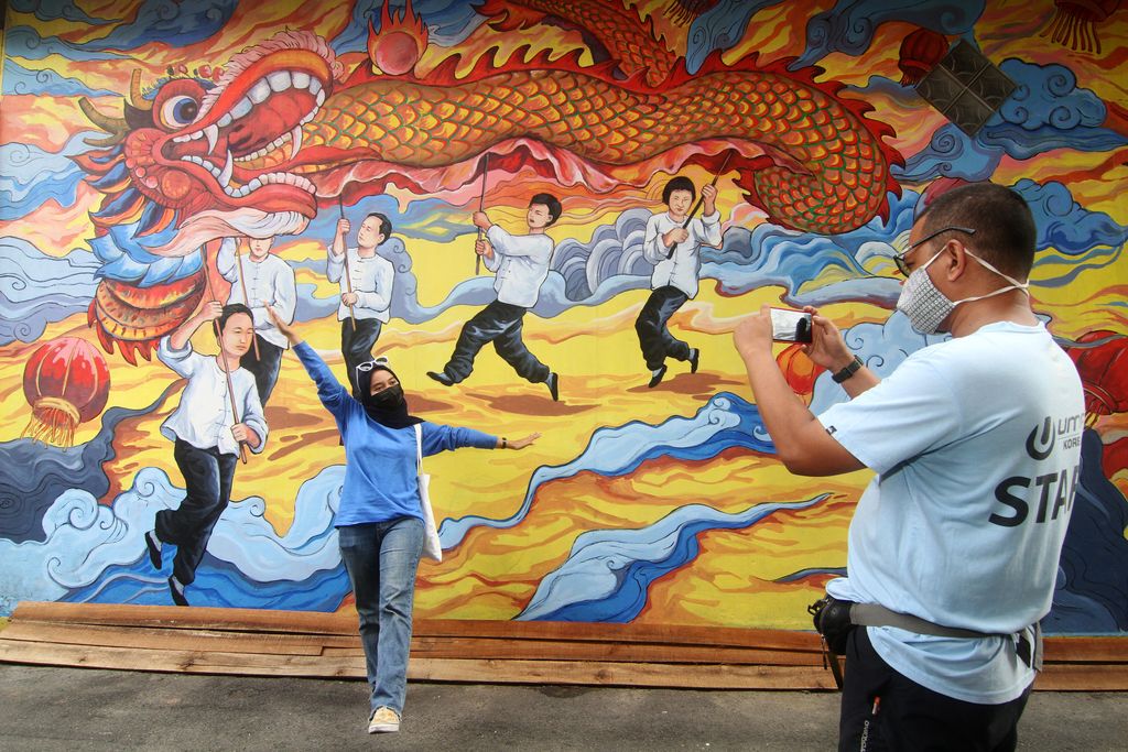 Seorang warga berpose di depan lukisan mural di dinding rumah toko di Gajahmada 9, Pontianak, Kalimantan Barat, Selasa (6/4/2021). Mural yang menggambarkan kesenian Tionghoa dan diinisiasi oleh pegiat seni Hervin Yulianto tersebut menjadi salah satu destinasi wisata baru di Kota Pontianak. ANTARA FOTO/Jessica Helena Wuysang/wsj.