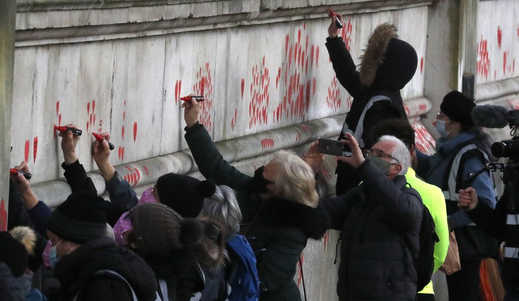 People paint red hearts onto the COVID-19 Memorial Wall mourning those who have died, along the embankment opposite the Houses of Parliament on the Embankment in London, Monday, April 5, 2021.  Hearts are being painted onto the wall in memory of the many thousands of people who have died in the UK from coronavirus. (AP Photo/Frank Augstein)