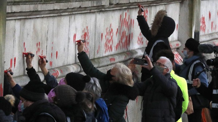Ribuan Hati Untuk Korban Corona di Inggis People paint red hearts onto the COVID-19 Memorial Wall mourning those who have died, along the embankment opposite the Houses of Parliament on the Embankment in London, Monday, April 5, 2021. Hearts are being painted onto the wall in memory of the many thousands of people who have died in the UK from coronavirus. (AP Photo/Frank Augstein)