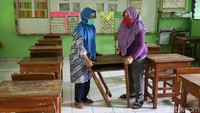 Dua orang guru menyiapkan meja untuk uji coba belajar tatap muka besok. Dalam proses belajar tatap muka ini, pihak sekolah menerapkan jaga jarak bagi para siswa.