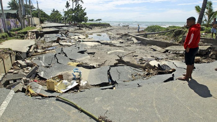 A woman walks along a road damaged by major flooding in Dili, East Timor, Tuesday, April 6, 2021. Several disasters brought on by severe weather in eastern Indonesia and neighboring East Timor have left a number of people dead or missing. (AP Photo/Kandhi Barnez)