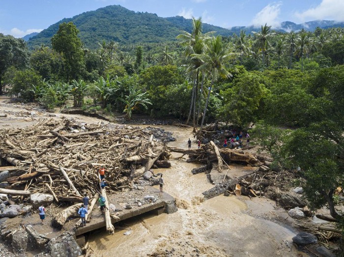Warga melewati tumpukan kayu-kayu yang menyumbat dan merusak salah satu jembatan penghubung antardesa di Adonara Timur, Kabupaten Flores Timur, Nusa Tenggara Timur (NTT), Rabu (7/4/2021). Menurut Organisasi Wahana Lingkungan Hidup Indonesia (Walhi), banjir bandang dan tanah longsor yang melanda di sejumlah wilayah di NTT dipicu kerusakan lingkungan akibat alih fungsi lahan, pertambangan, dan pembalakan liar. ANTARA FOTO/Aditya Pradana Putra/hp.