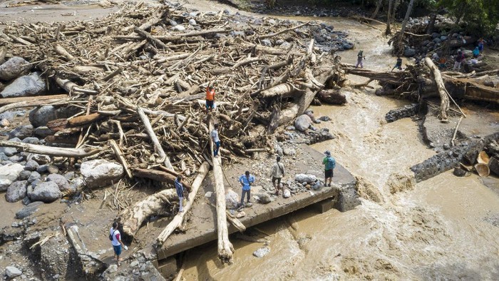 Warga melewati tumpukan kayu-kayu yang menyumbat dan merusak salah satu jembatan penghubung antardesa di Adonara Timur, Kabupaten Flores Timur, Nusa Tenggara Timur (NTT), Rabu (7/4/2021). Menurut Organisasi Wahana Lingkungan Hidup Indonesia (Walhi), banjir bandang dan tanah longsor yang melanda di sejumlah wilayah di NTT dipicu kerusakan lingkungan akibat alih fungsi lahan, pertambangan, dan pembalakan liar. ANTARA FOTO/Aditya Pradana Putra/hp.