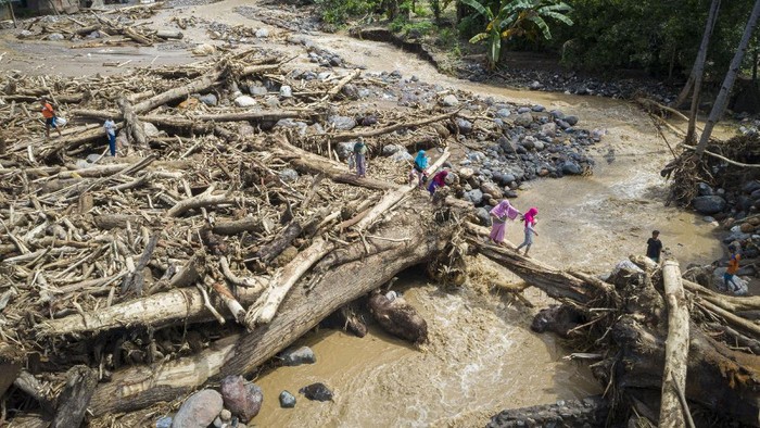 Gelondongan Kayu Menumpuk Sisa Banjir Bandang di NTT Warga melewati tumpukan kayu-kayu yang menyumbat dan merusak salah satu jembatan penghubung antardesa di Adonara Timur, Kabupaten Flores Timur, Nusa Tenggara Timur (NTT), Rabu (7/4/2021). Menurut Organisasi Wahana Lingkungan Hidup Indonesia (Walhi), banjir bandang dan tanah longsor yang melanda di sejumlah wilayah di NTT dipicu kerusakan lingkungan akibat alih fungsi lahan, pertambangan, dan pembalakan liar. ANTARA FOTO/Aditya Pradana Putra/hp.