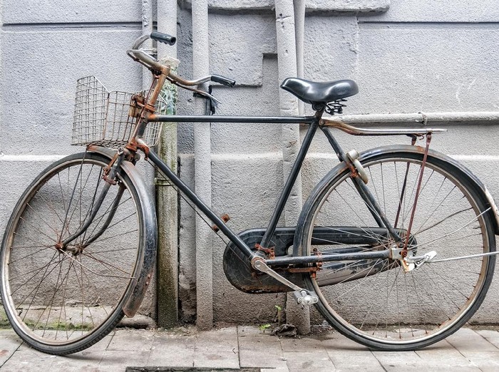 gowes sepeda Old and rusty bicycle parked against a gray city wall