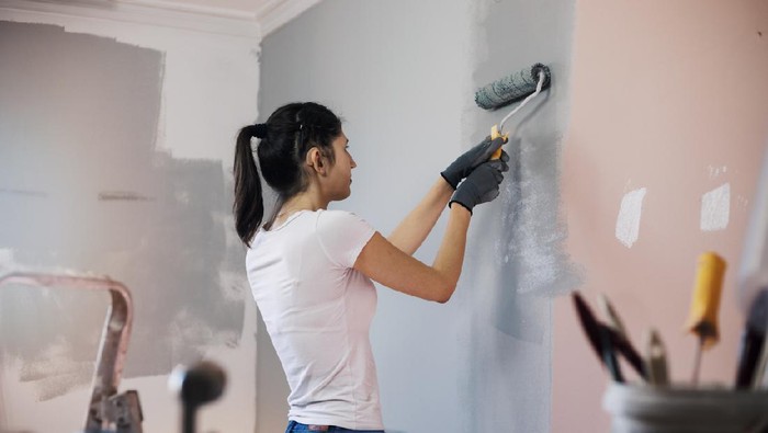 Young woman with hearing aid, during reconstruction of apartment, enjoying while painting her walls