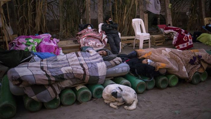 A man sleeps on top of empty oxygen cylinders that stretch across a dirt road, as people wait for a shop to open in order to refill their tanks, in the Villa El Salvador neighborhood, as the lack of medical oxygen to treat COVID-19 patients continues in Lima, Peru, Tuesday, April 6, 2021. (AP Photo/Rodrigo Abd)