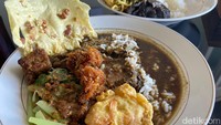 Dalam semangkuk pecel rawon terlihat nasi direndam kuah rawon cukup banyak. Pelengkapnya pecel sayur yang disirami sambal kacang. Lauk pendampingnya ada peyek udang, empal sapi, ragi kelapa, paru goreng dan peyek kacang.