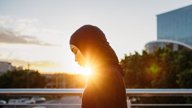 olahraga pagi Arabic woman runner outdoors in the morning with bright sunlight. Side view of young muslim woman wearing hijab resting after workout outdoors in the city.