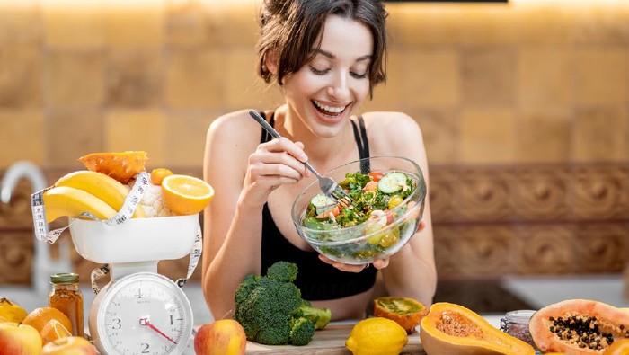 Sports woman eating salad, standing with lots of healthy fresh food on the kitchen. Concept of losing weight, sports and healthy eating