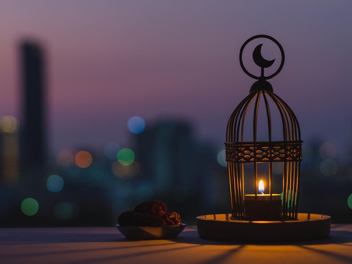 Lantern that have moon symbol on top and small plate of dates fruit with dusk sky and city bokeh light background for the Muslim feast of the holy month of Ramadan Kareem.