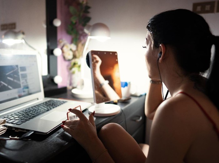 The woman sitting watching on a laptop while make-up at home alone