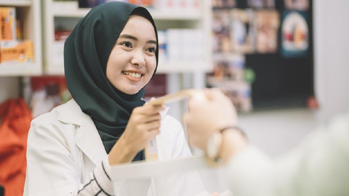 an asian muslim lady cashier take over the basket from her customer for check out payment