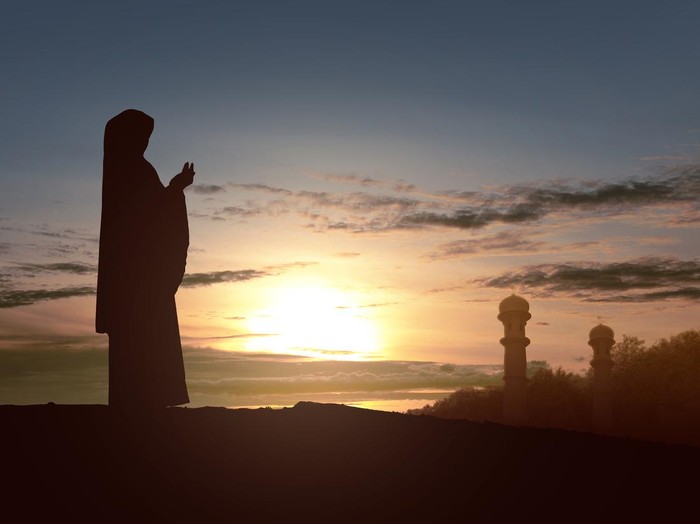 Arab woman with veil against orange yellow sky