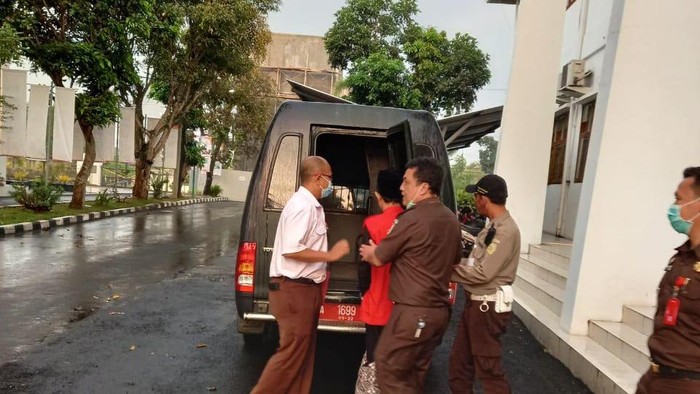 Tersangka bersarung menggunakan rompi saat digiring ke mobil tahanan.