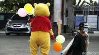 Terlihat badut Winny The Pooh tersebut berdiri di pintu keluar SPBU. Kedua tangannya memegang balon warna-warni.